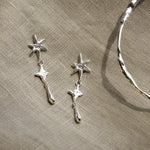 Silver star-shaped earrings and silver bangle on a beige fabric background