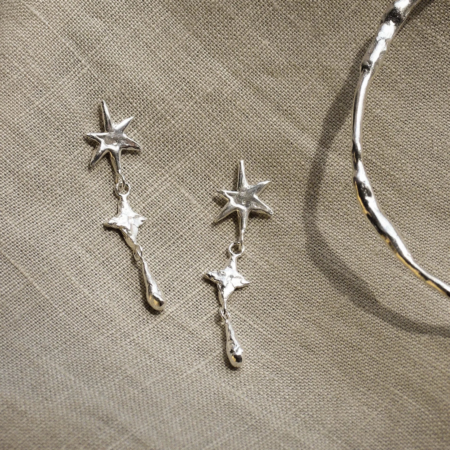 Silver star-shaped earrings and silver bangle on a beige fabric background