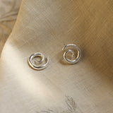 Pair of silver spiral earrings on a beige fabric background