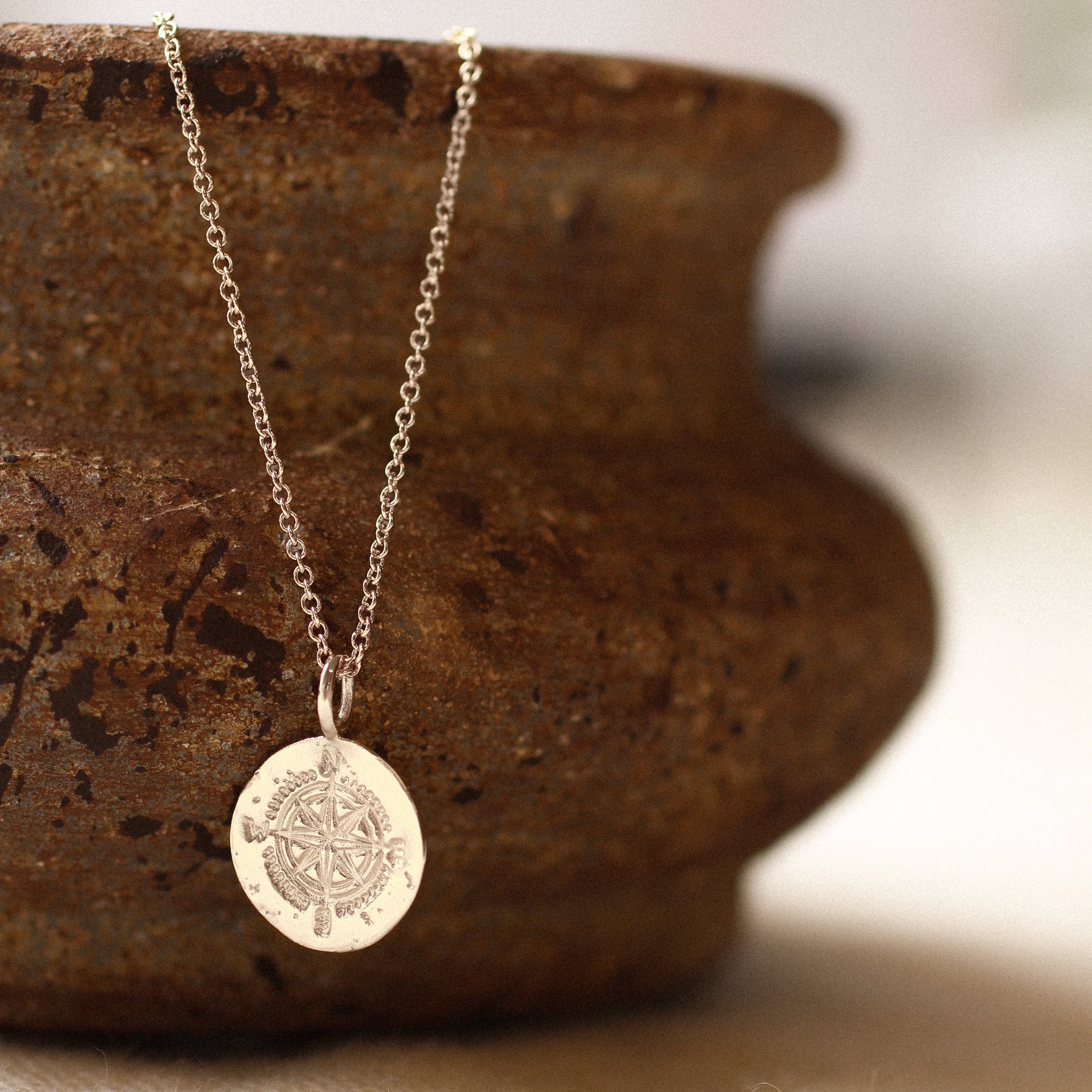 silver compass necklace with round pendant handing on a ceramic textured bowl