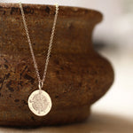 silver compass necklace with round pendant handing on a ceramic textured bowl