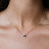 A close-up of a delicate gold chain necklace worn by a model, featuring a greeny blue sapphire and pear shaped diamond.