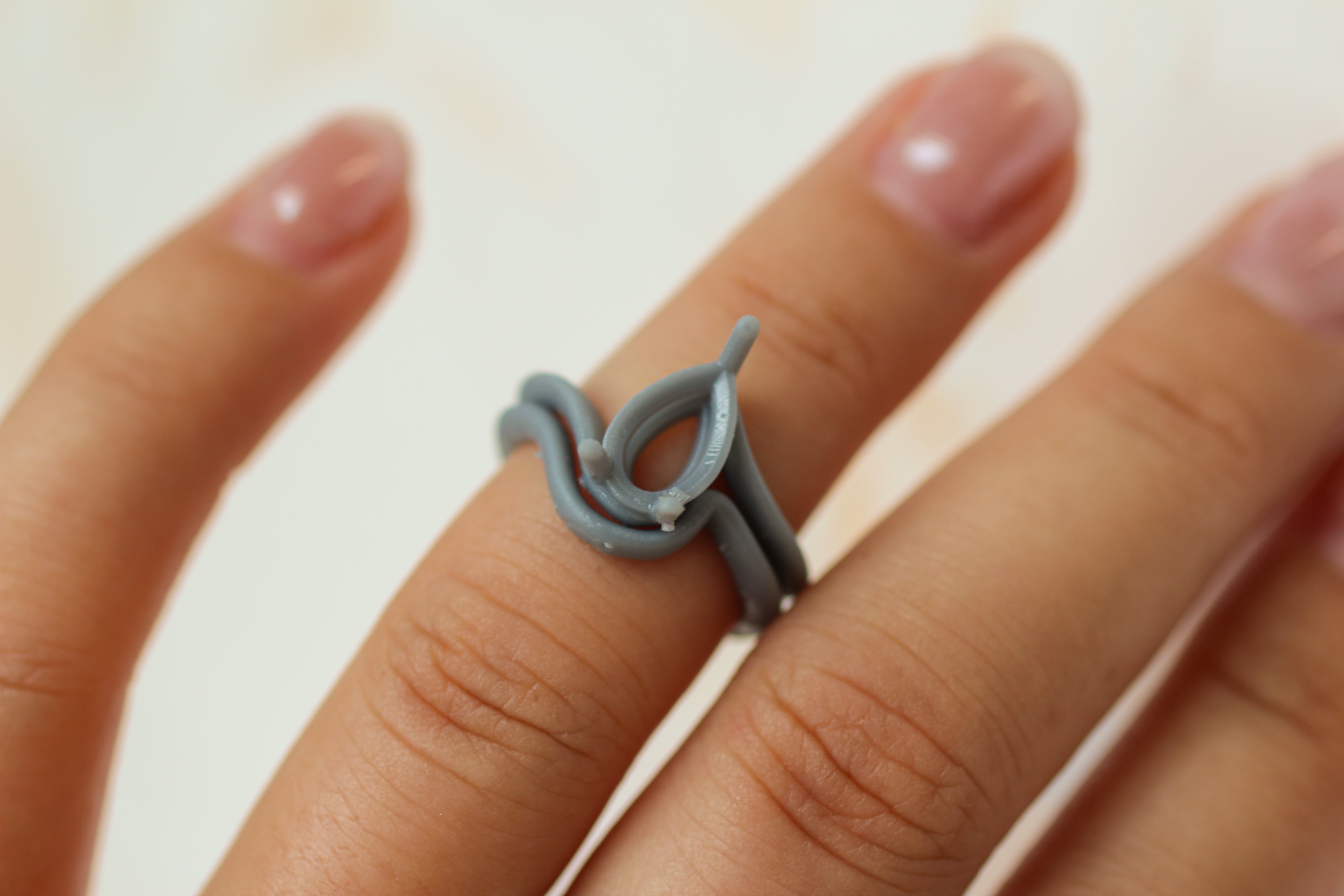 A close-up of a hand wearing a gray resin ring with an organic, flowing loop design.