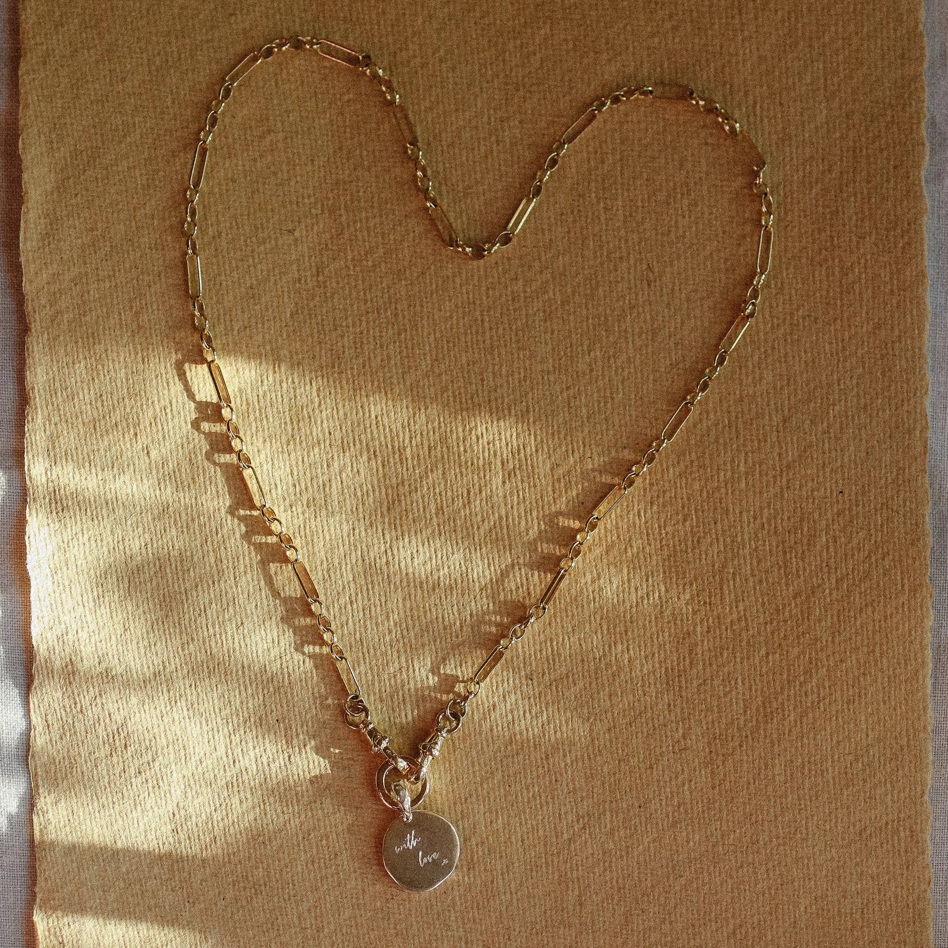 Gold chain necklace with a heart-shaped pendant on a textured brown background