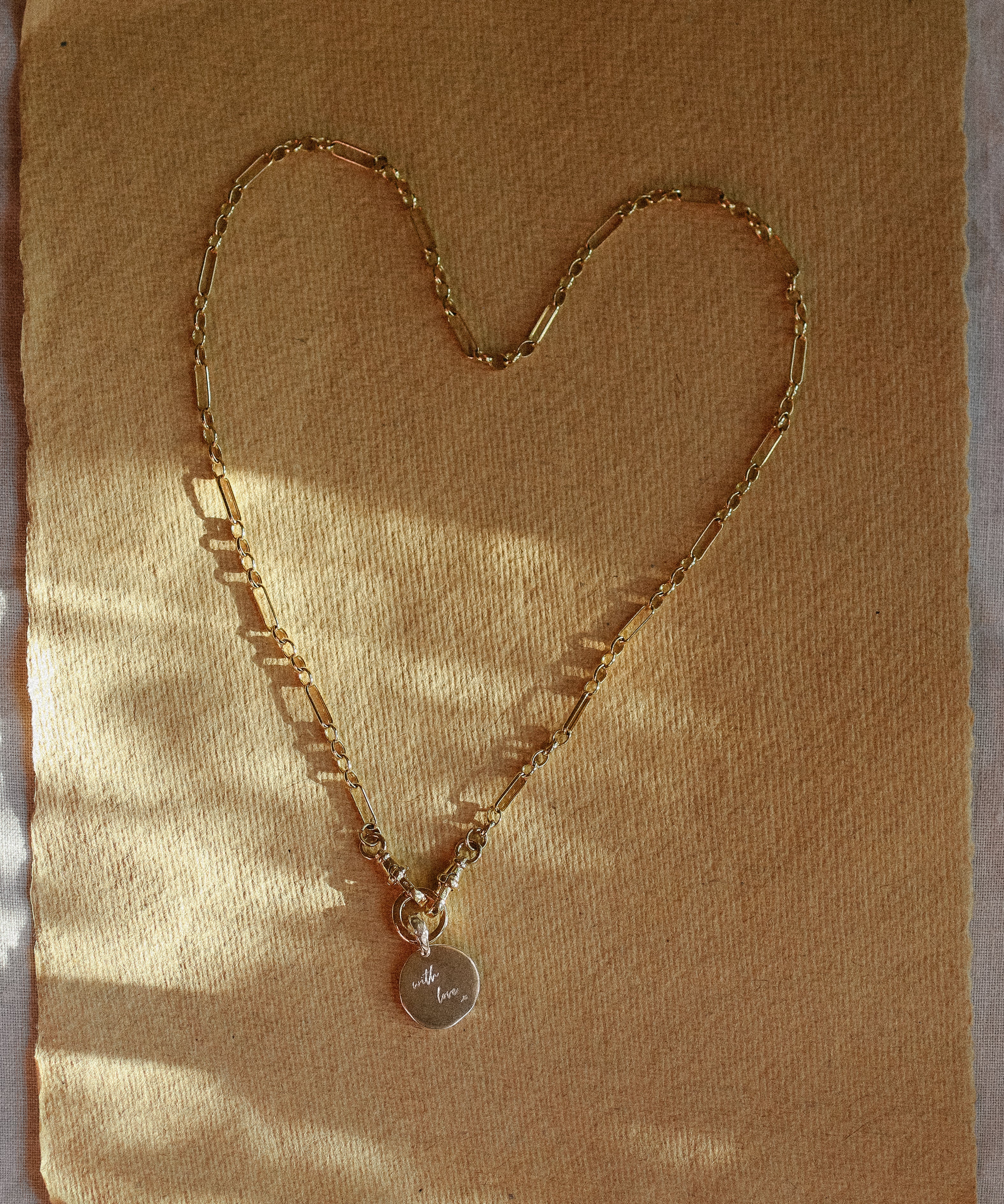 Gold chain necklace with a heart-shaped pendant on a textured brown background