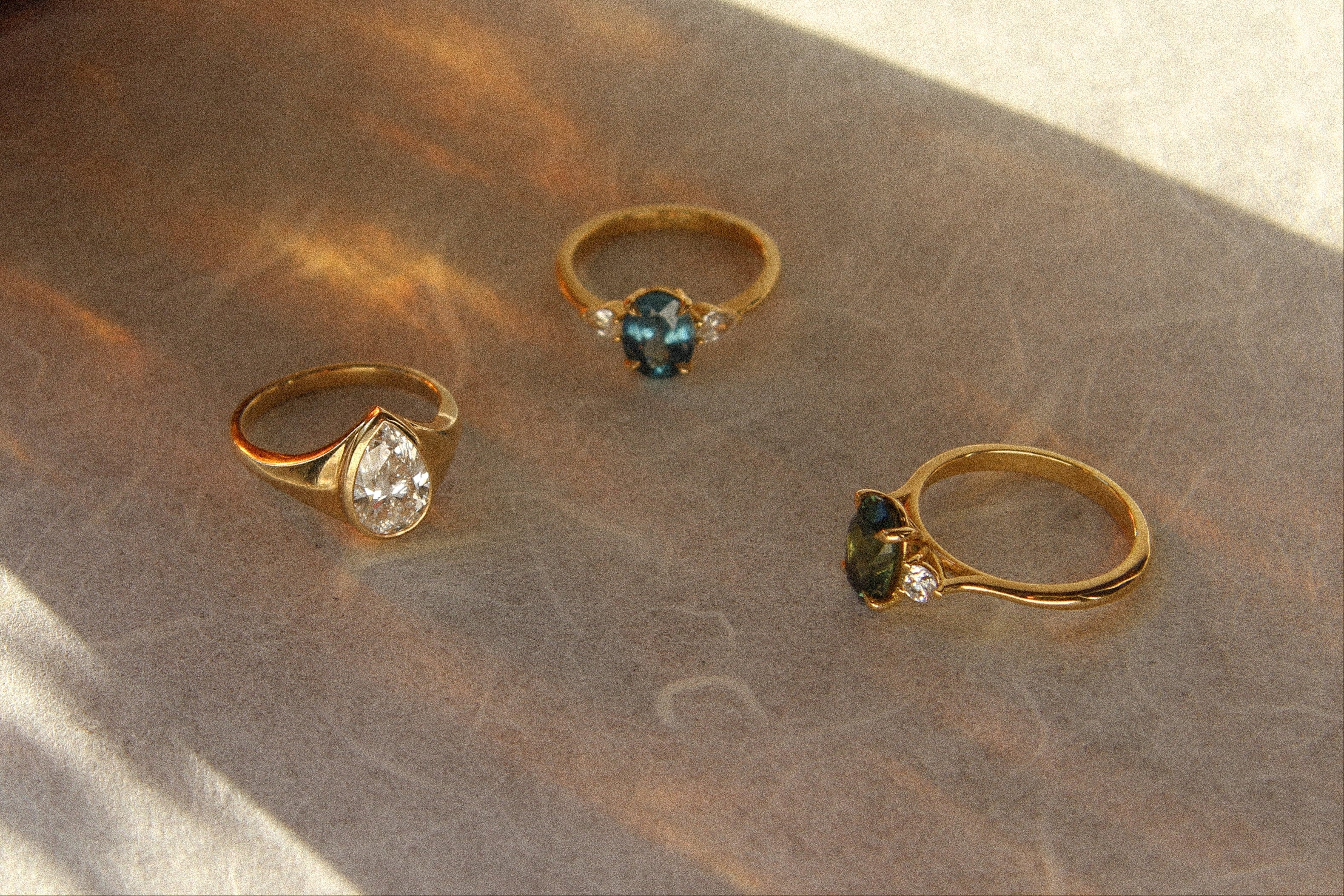 three gold engagement rings with diamonds, blue sapphire and green sapphire with warm shadow