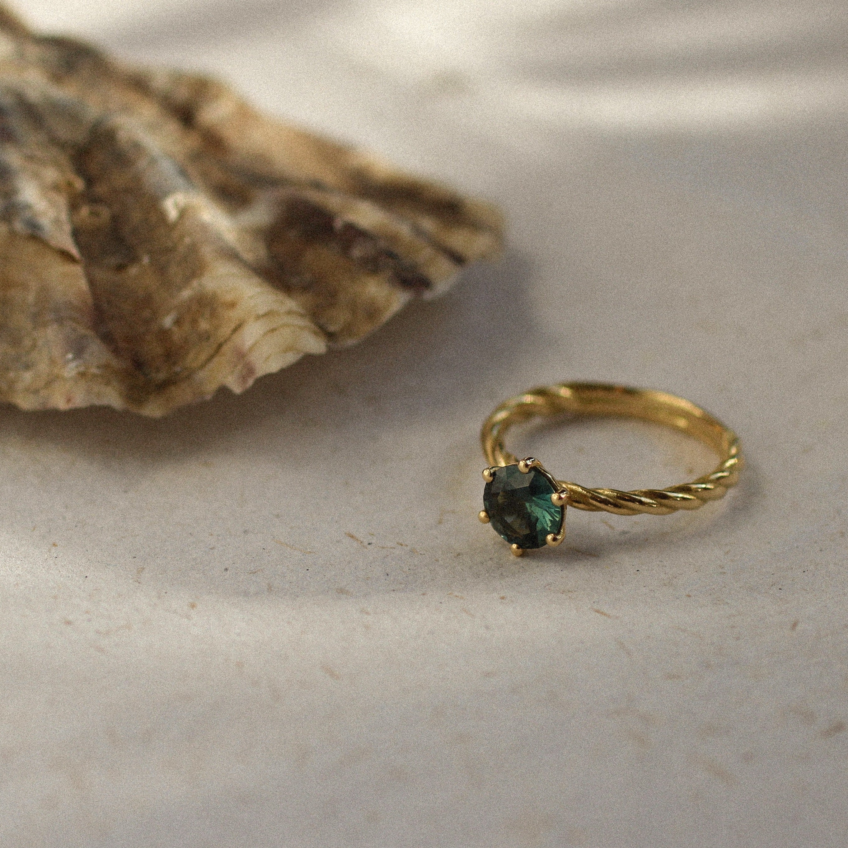 twisted blue sapphire engagement ring next to an oyster shell