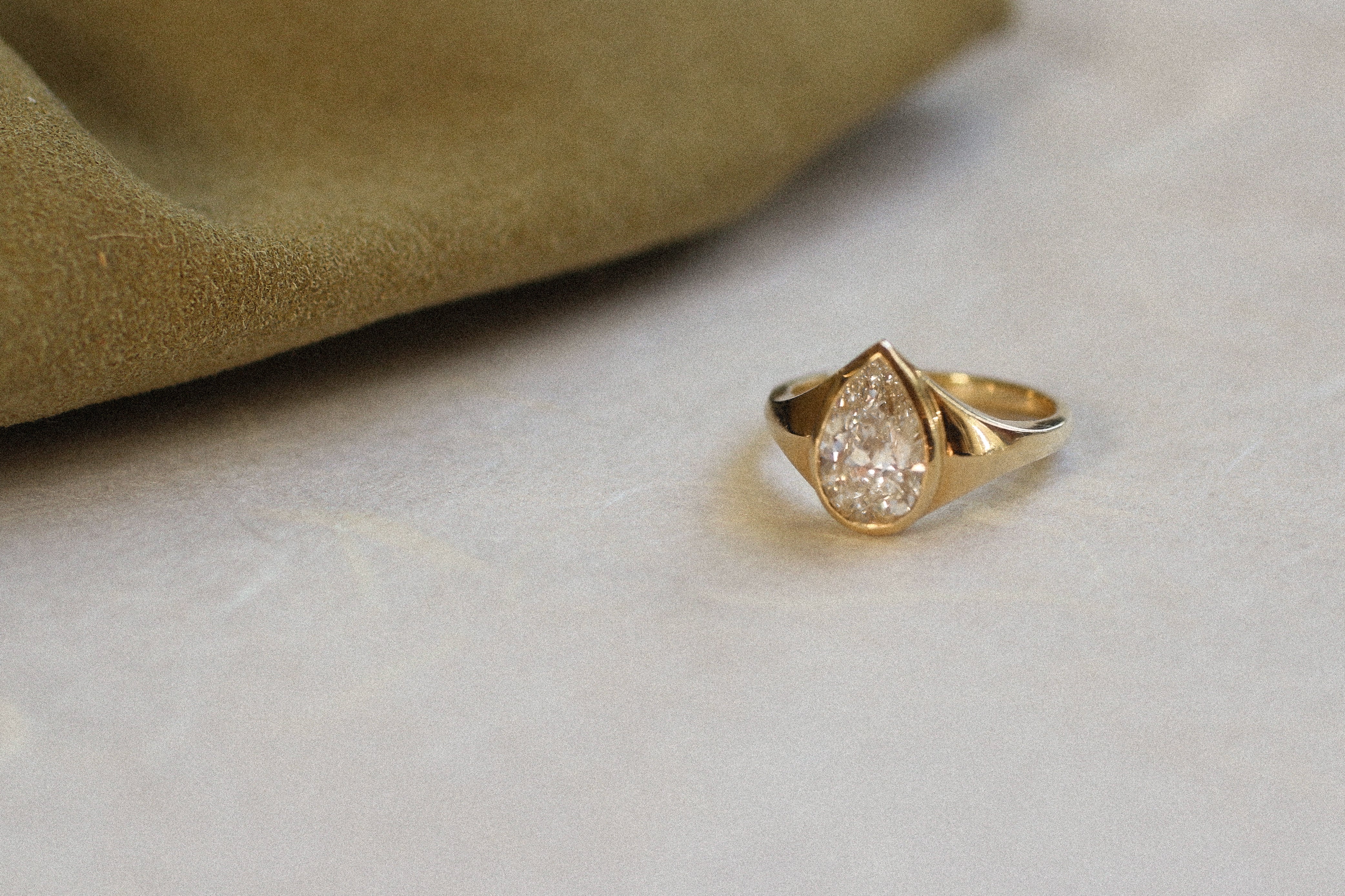 Gold bezel engagement ring with pear diamond on a light background