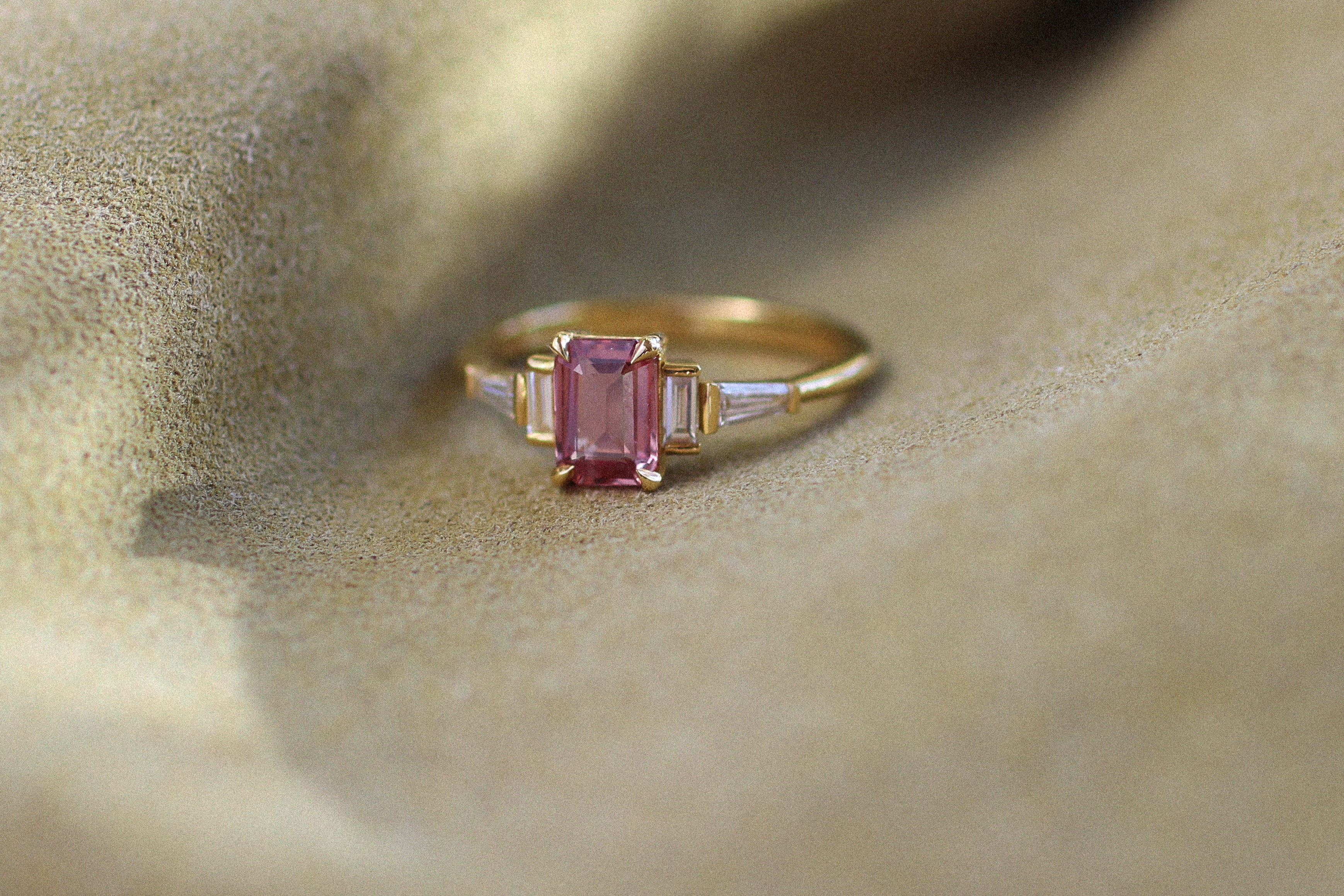 Gold ring with a pink gemstone on a textured beige surface