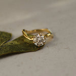 Gold ring with a diamond on a green leaf against a beige background