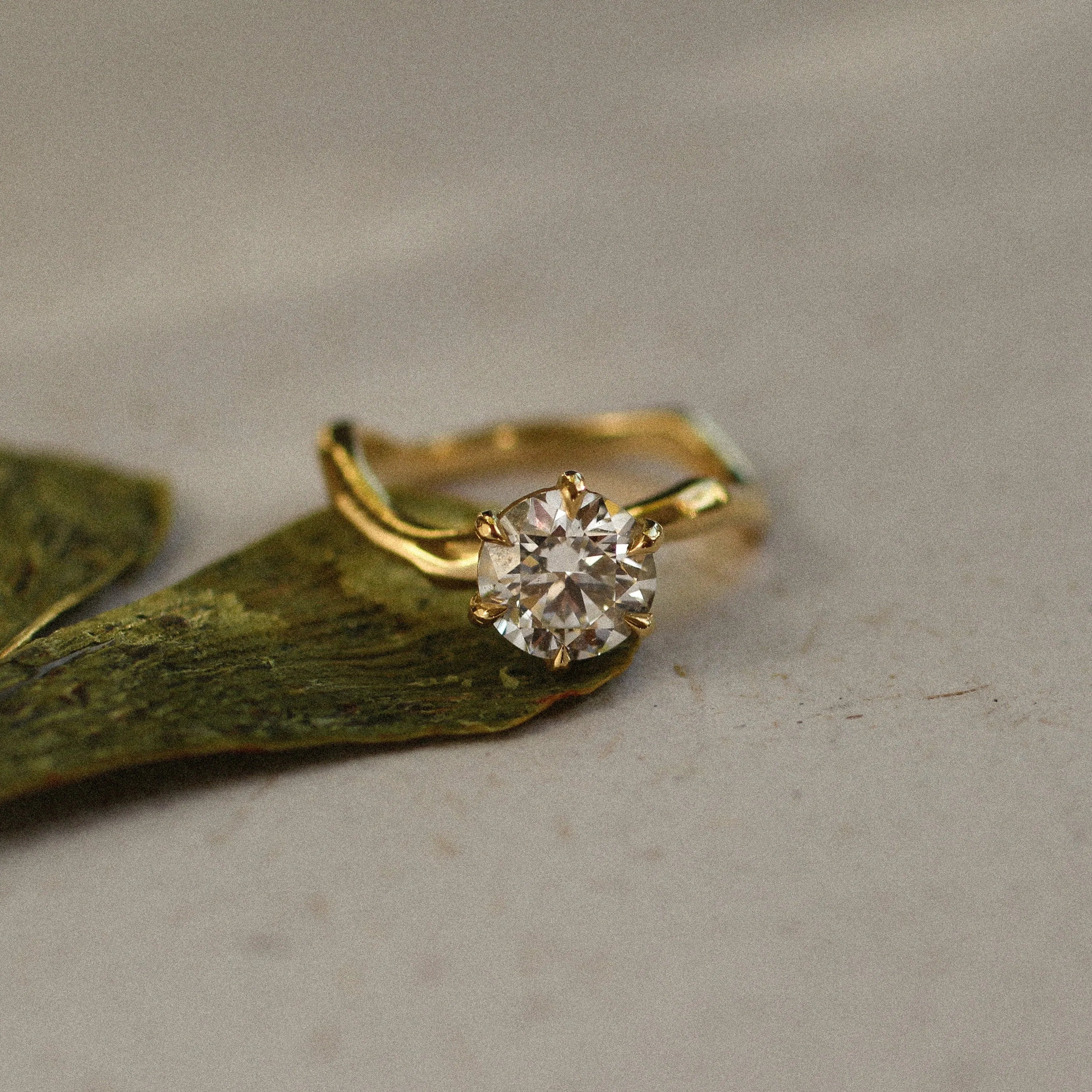 Gold ring with a diamond on a green leaf against a beige background