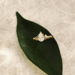 Gold ring with a diamond on a green leaf against a textured beige background