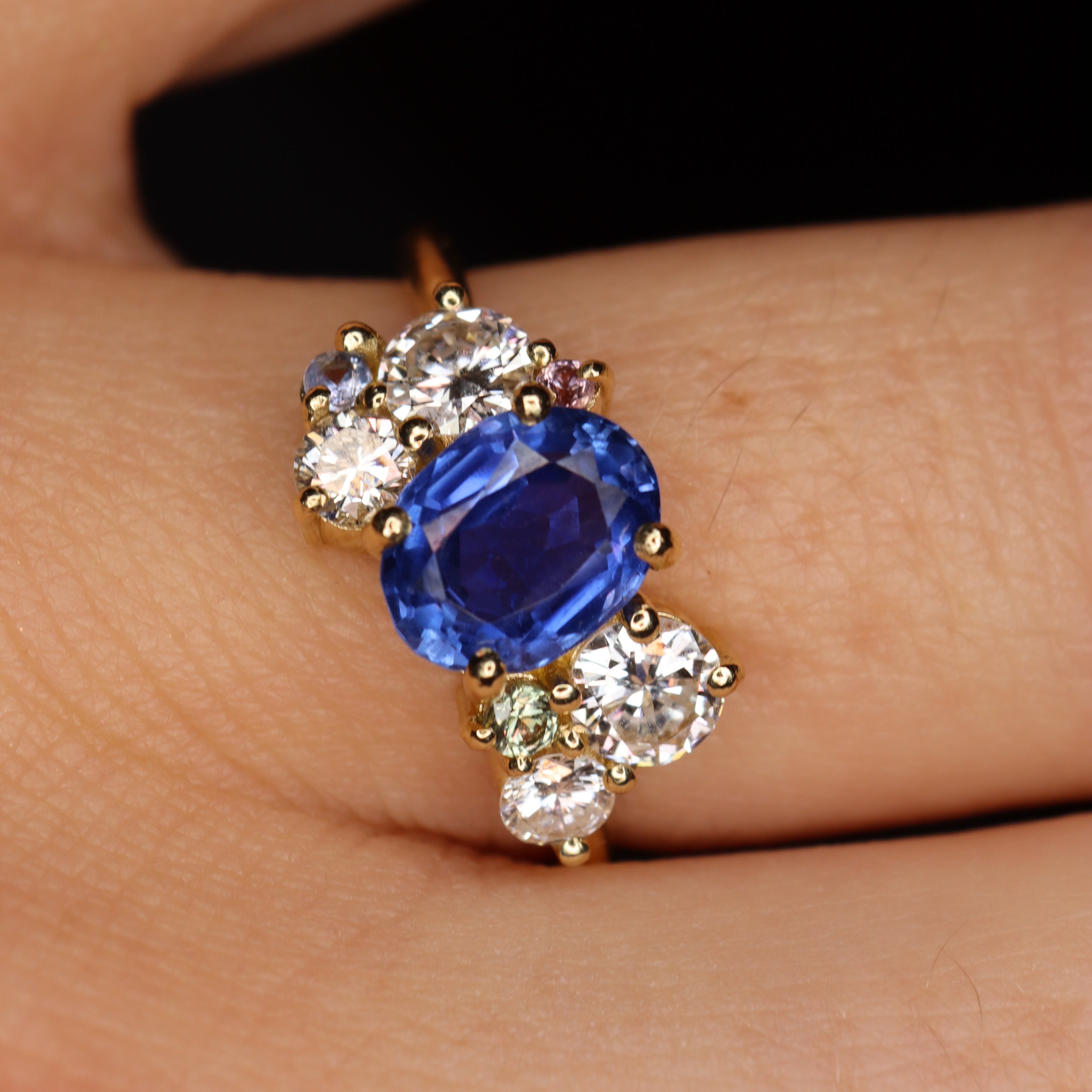 Close-up of a ring with a blue gemstone and diamonds on a person's finger.