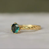 round sapphire engagement ring with twisted band on a neutral surface