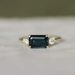 Ring with a blue gemstone set east-west and diamonds on a white surface