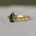 engagement ring with star set diamonds in the gold band and a green pear sapphire
