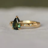 engagement ring with star set diamonds in the gold band and a green pear sapphire