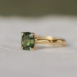 green sapphire engagement ring with gold wobbly organic band with a blurred background