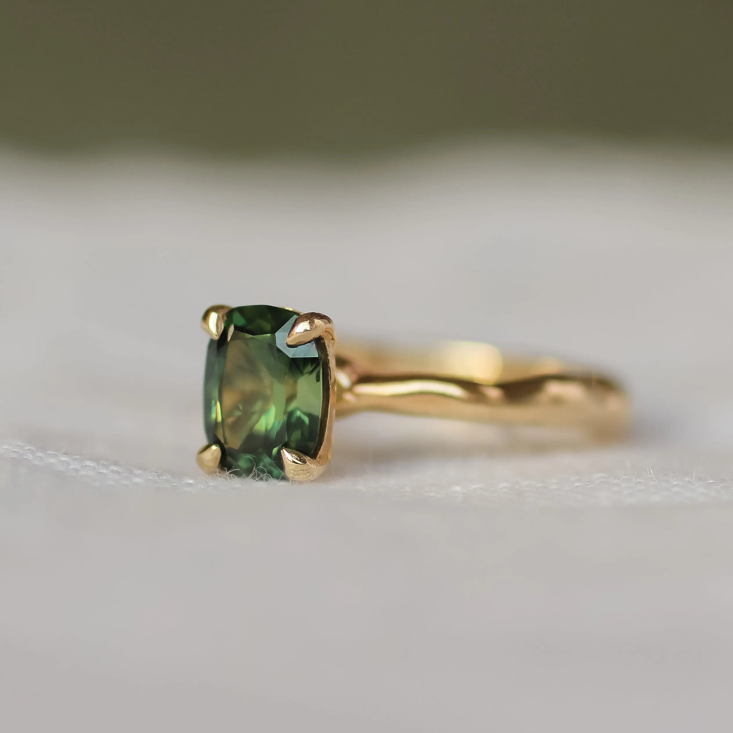 green sapphire engagement ring with gold wobbly organic band with a blurred background