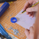 Hand holding pencil sketching a ring, next to a wax mould in the same shape