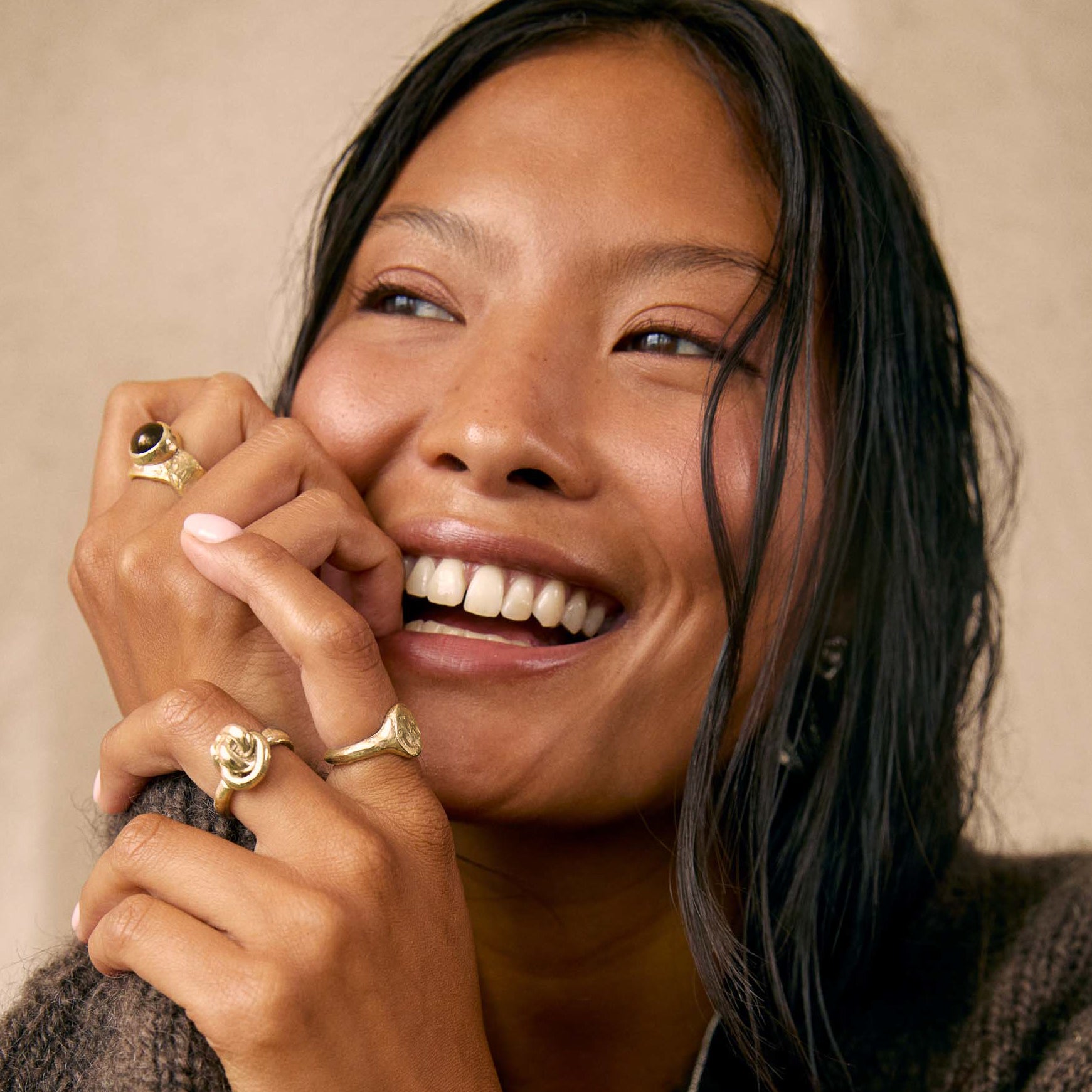 model with black wet hair smiling and wearing three chunky gold rings in smoky quartz, knot and oval signet designs