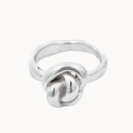 A sterling silver ring featuring a knotted design on a smooth, polished band, set against a plain off-white background.
