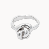 A sterling silver ring featuring a knotted design on a smooth, polished band, set against a plain off-white background.
