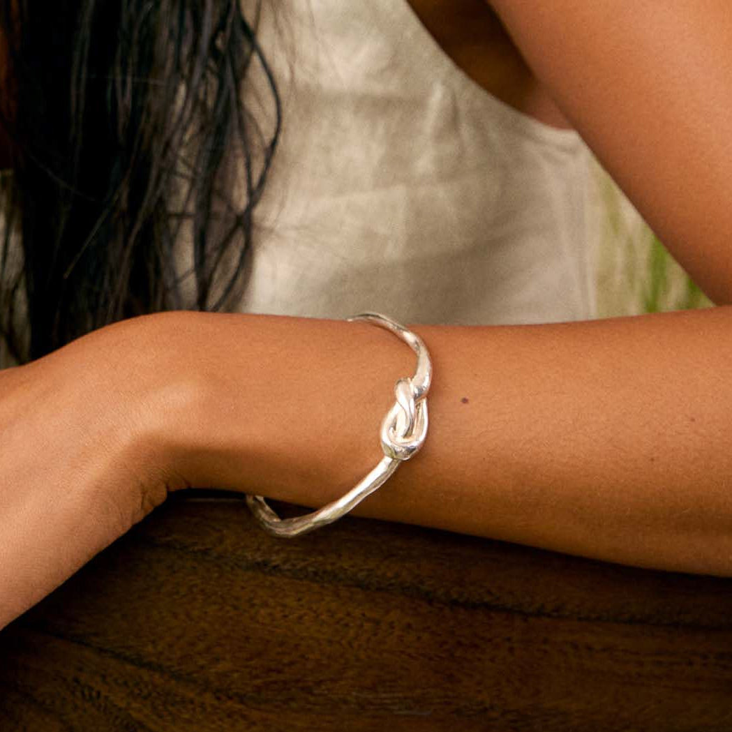 close up of an arm resting on a wooden chair wearing a chunky molten silver knot bangle