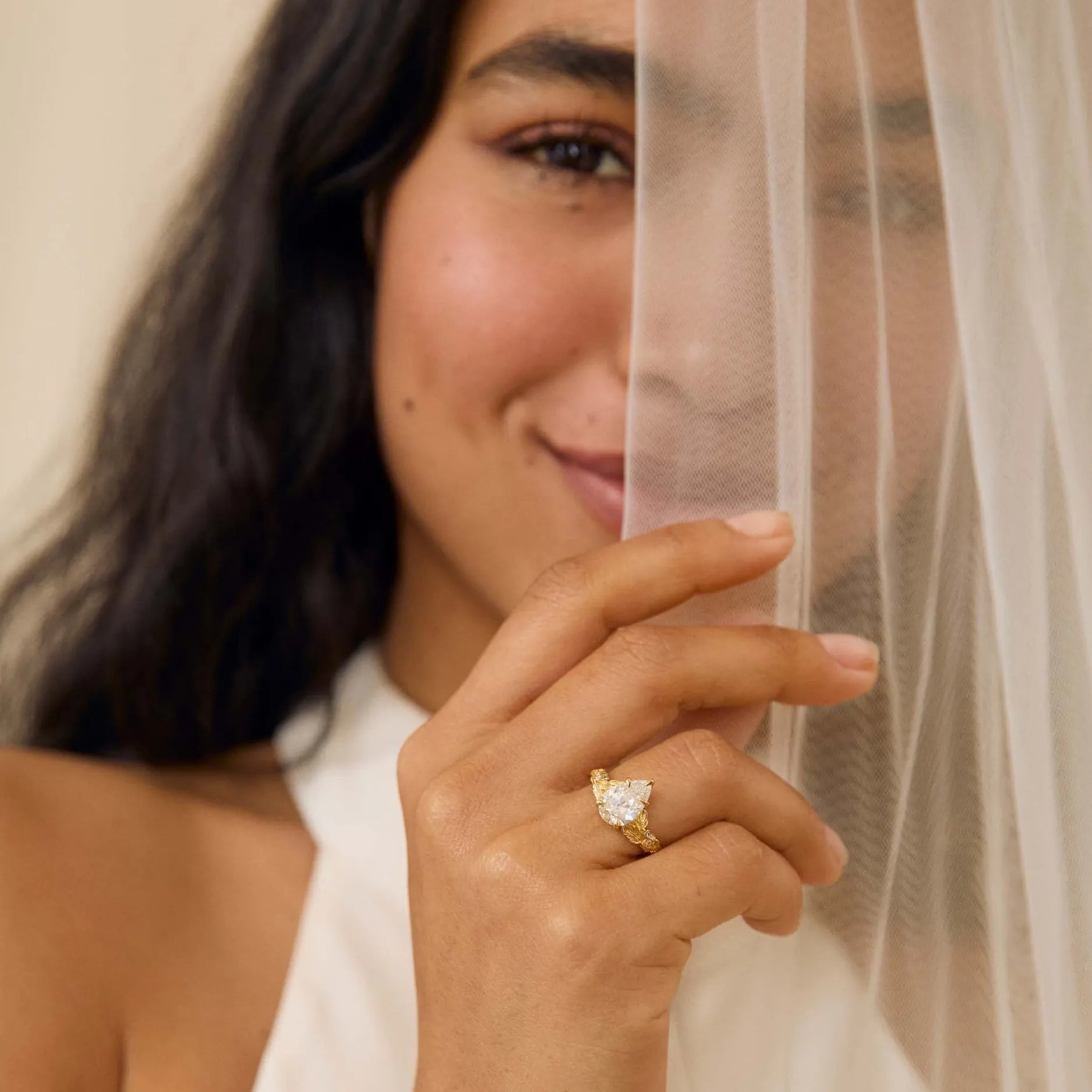 model wearing a leaf-detailed pear diamond engagement ring hiding before a veil