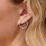 A woman shown in side profile wearing a delicate silver circle stud earring, with long blonde wavy hair.
