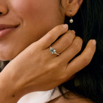 Woman wearing a light blue sapphire engagement ring in white gold and earring blurred in the background