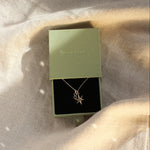 gold necklace with star and '8' pendant in a green gift box on neutral fabric