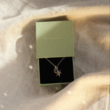 gold necklace with star and '8' pendant in a green gift box on neutral fabric