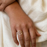 hand wearing a gold s-shaped ring against a neutral fabric
