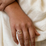 hand wearing a gold s-shaped ring against a neutral fabric