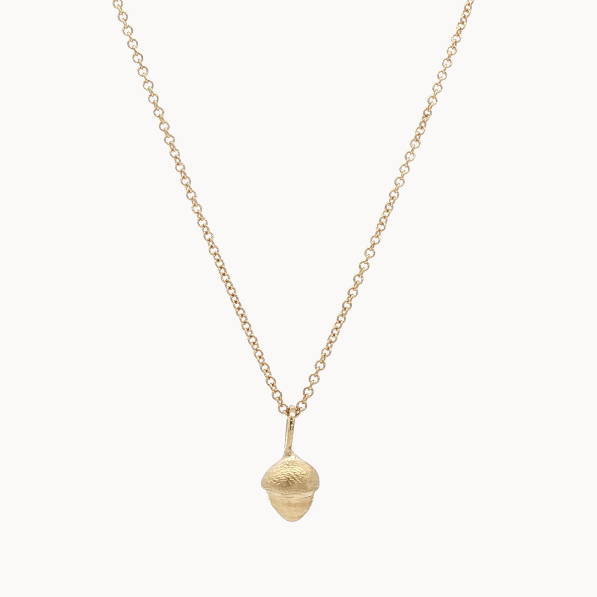 Gold necklace with a small acorn pendant on a white background
