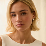 Woman with blonde hair wearing white gold sun shaped bridal earrings, a white high neck dress against a beige background