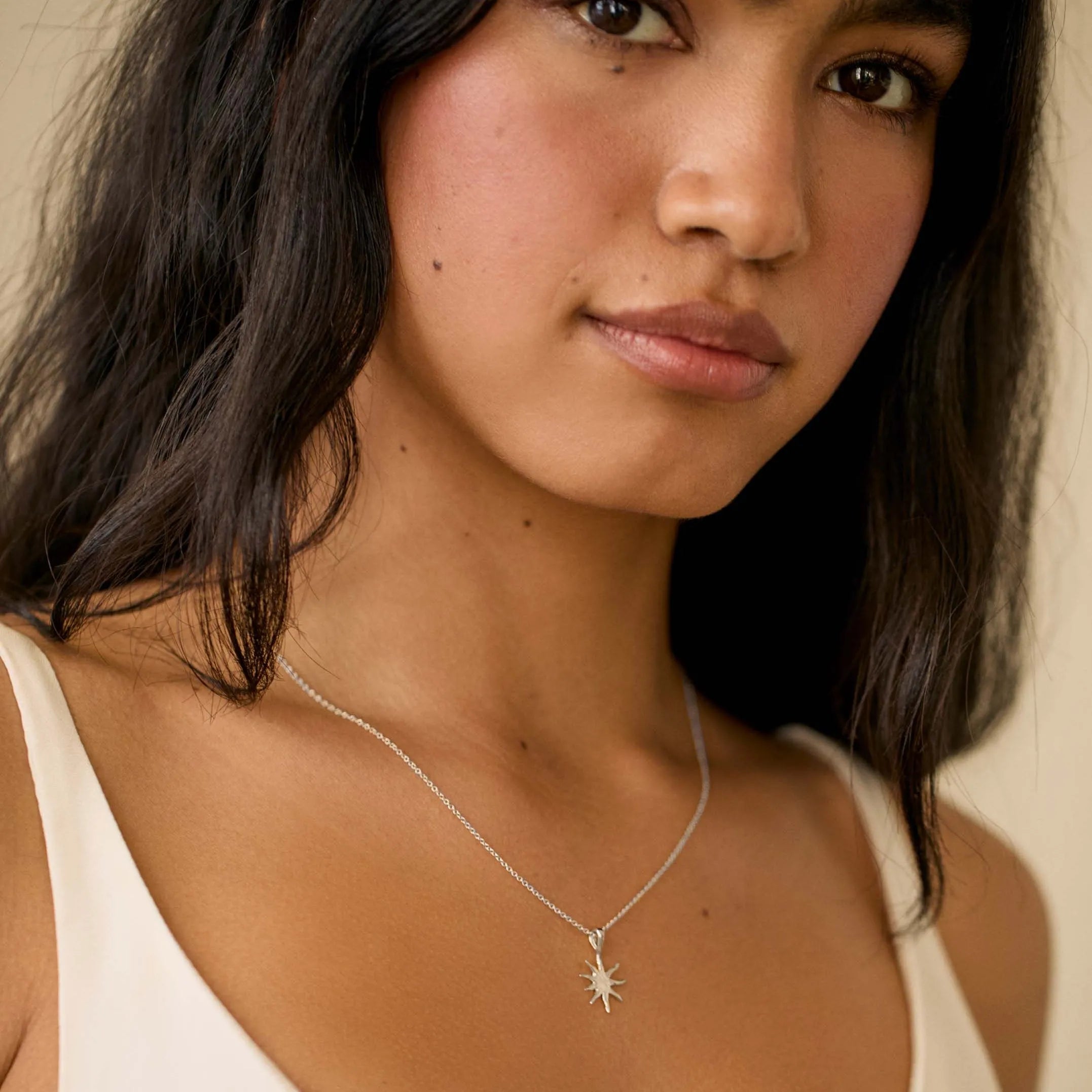 woman wearing white strappy top and white gold mini sun pendant necklace