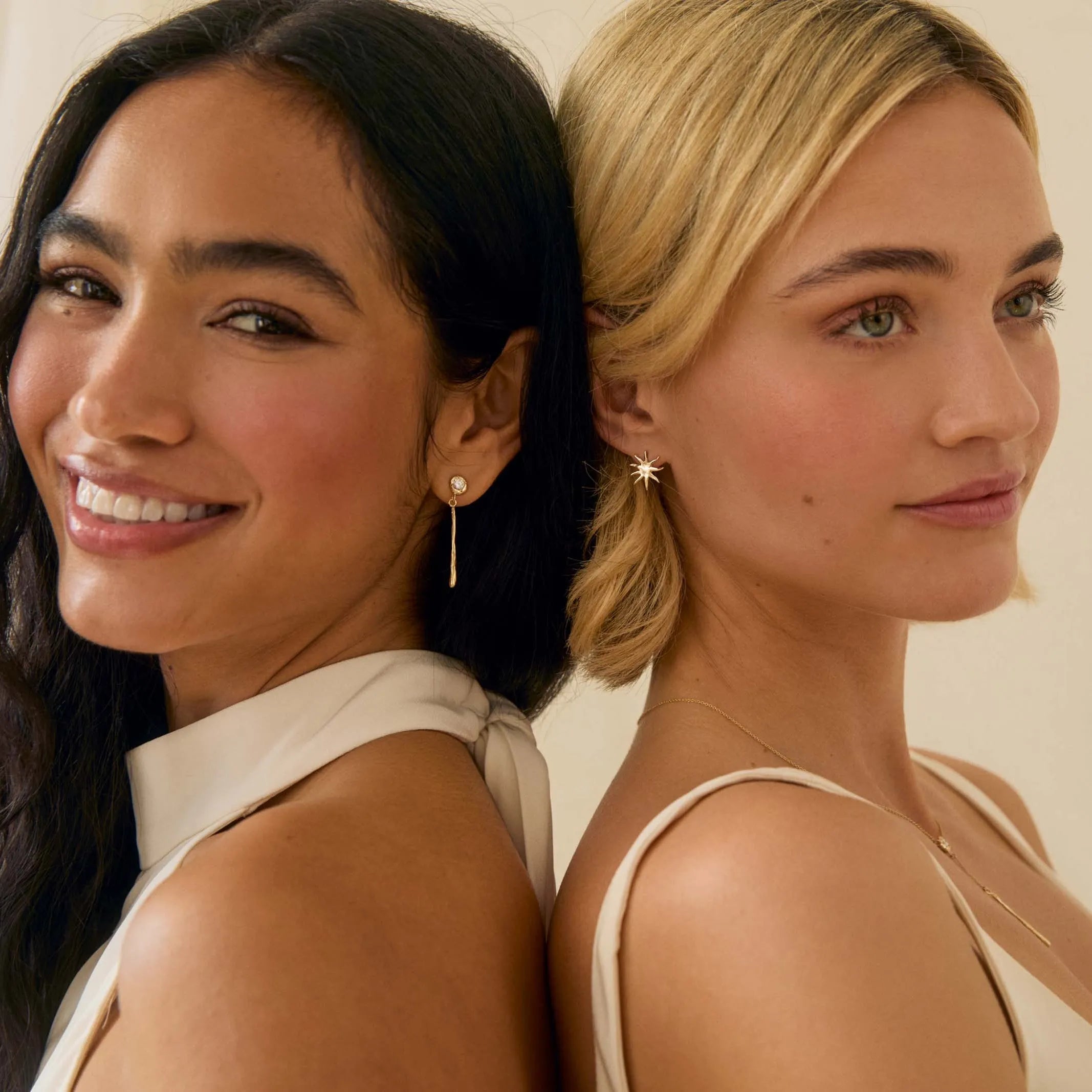 a brunette and blonde model back to back wearing bridal jewellery smiling to camera