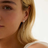 Close-up of a woman wearing white gold diamond dangle earrings with a blurred background