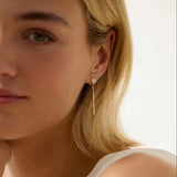 Close-up of a woman wearing gold diamond earrings with molten drop detail a blurred background