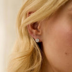 Close-up of a person wearing a white gold diamond stud earring with blonde hair.