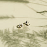 Two small gold hoop-style earrings resting on a warm beige surface with soft shadows cast across the scene.
