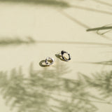 Two small gold hoop-style earrings resting on a warm beige surface with soft shadows cast across the scene.