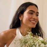 Smiling woman wearing diamond star dangle earrings and  holding a bouquet of flowers with a plain background