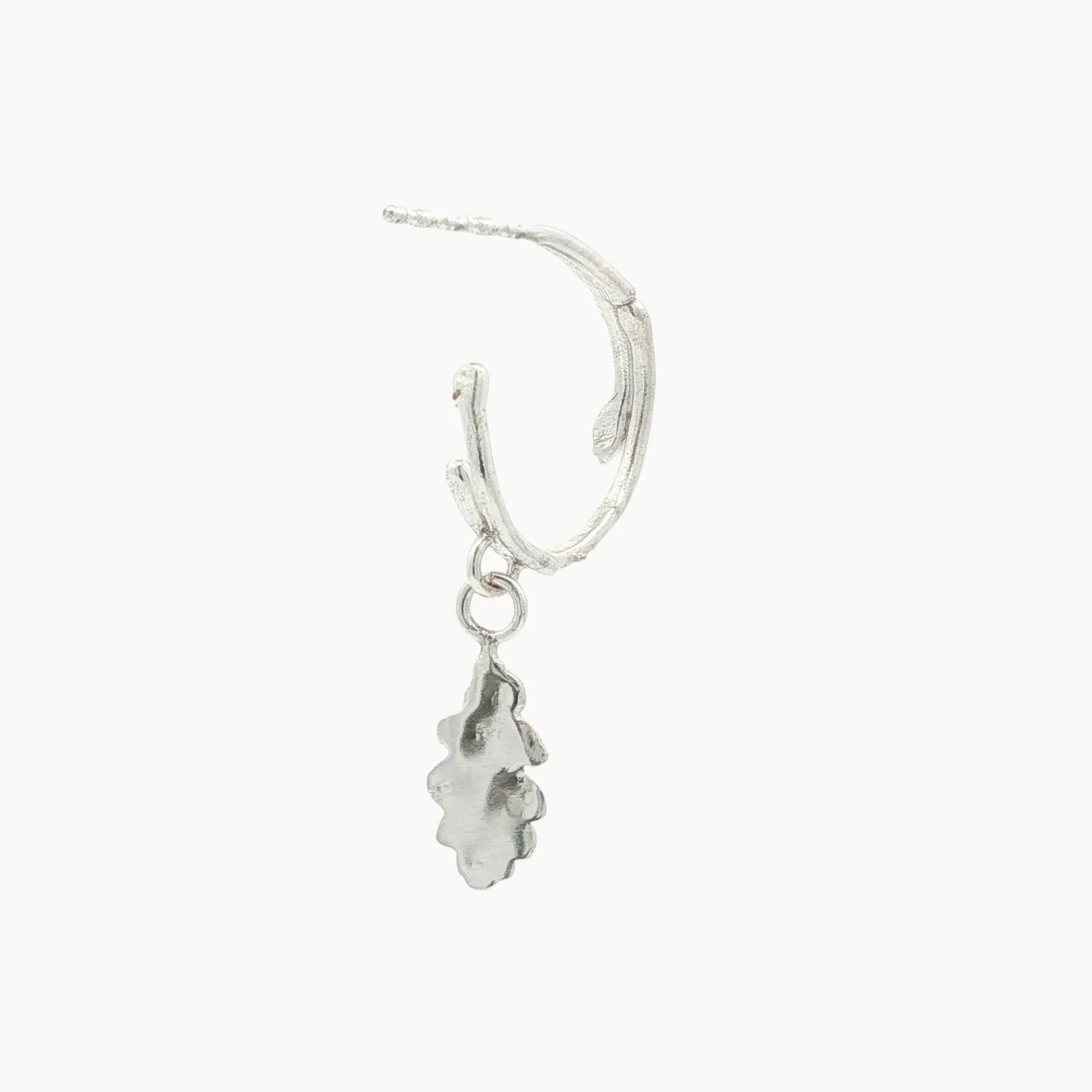 Silver hoop earring with a small dangling silver oak charm on a white background