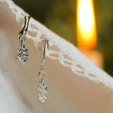 silver hoops with oak leaf pendants on lace fabric with blurred candle in background