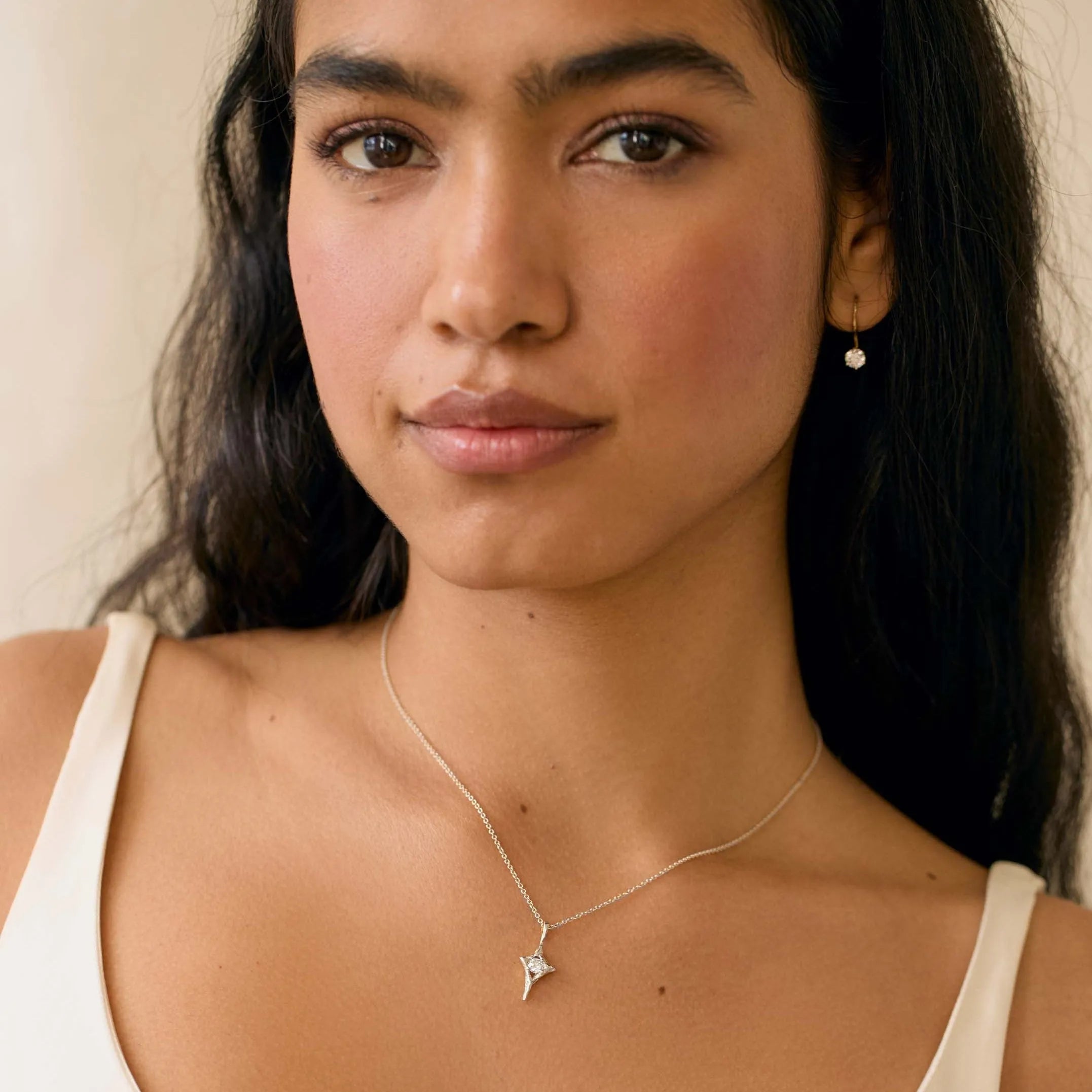 woman wearing strappy white top wearing hite gold star diamond necklace and diamond hook earrings