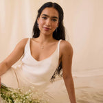 Woman in a white dress, wearing star dangle earrings and four-point star necklace, holding flowers against a neutral background