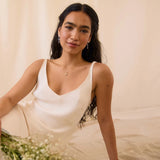 Woman in a white dress, wearing star dangle earrings and four-point star necklace, holding flowers against a neutral background